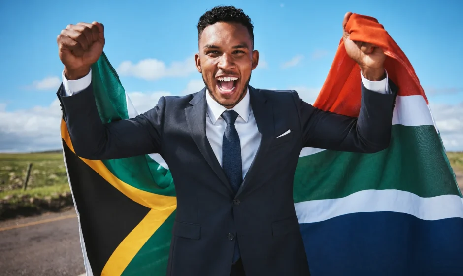 Man in a business suit holding the South African flag while celebrating South African citizenship by naturalisation
