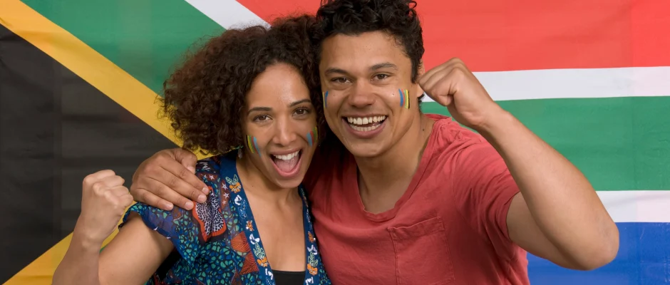Couple celebrating in front of the South African flag for a guide to South African permanent residence requirements