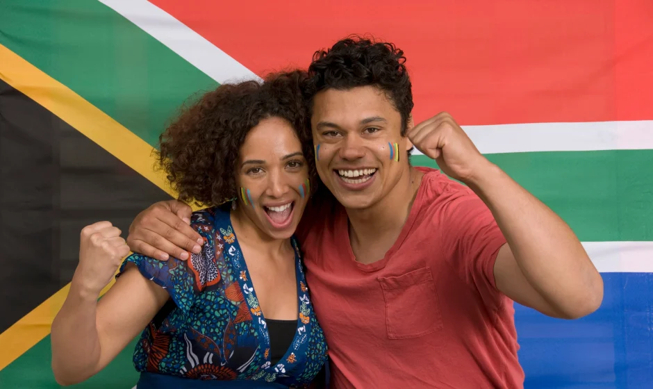 Couple celebrating in front of the South African flag for a guide to South African permanent residence requirements
